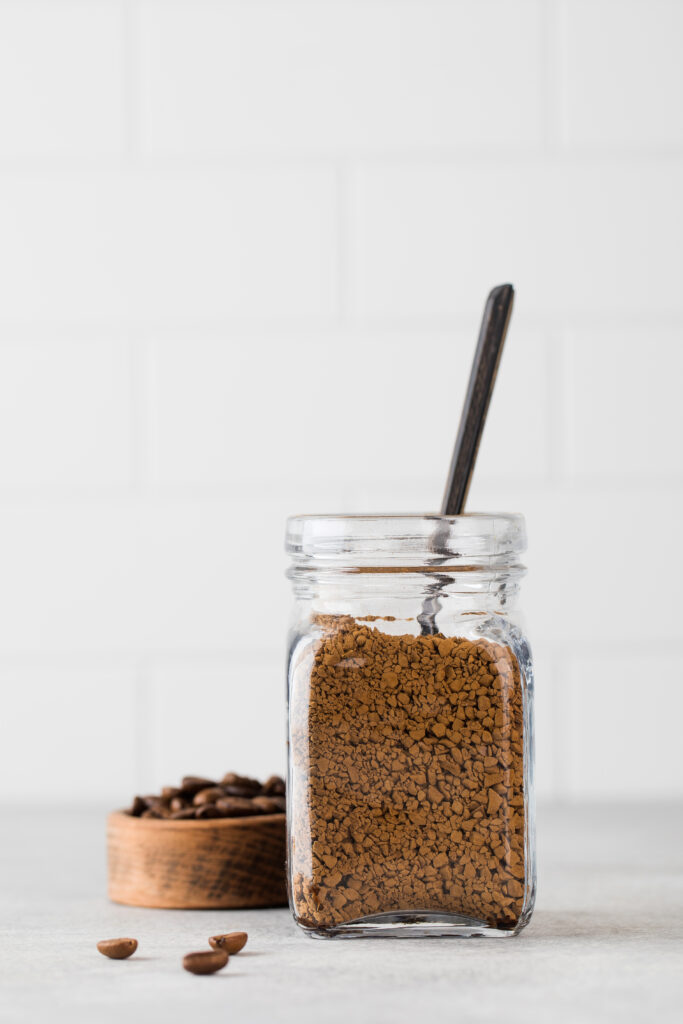A glass jar with instant coffee and a teaspoon.